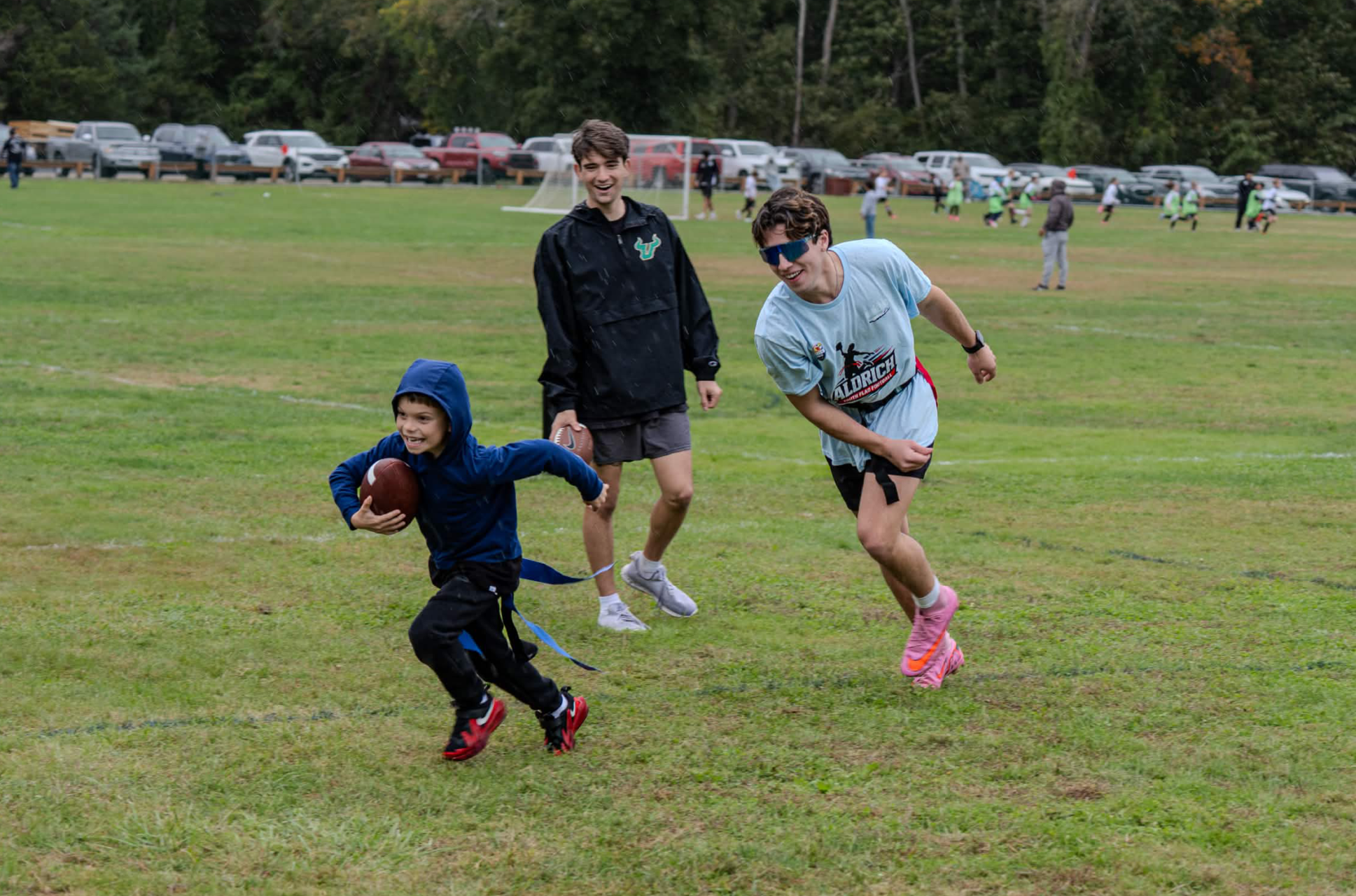 A child and two young people enjoying a game of football together on a grassy field